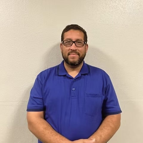 Portrait of a man wearing glasses and a blue polo shirt against a white wall