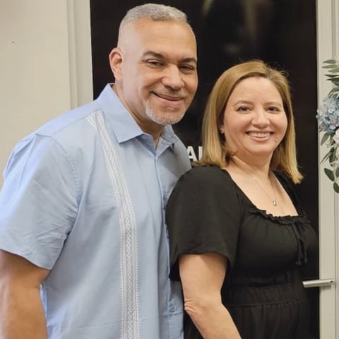 Man in light blue shirt and woman in black top smiling together at an indoor event