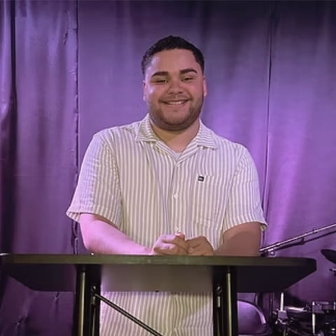 Man in striped shirt smiling while playing keyboard against purple stage background