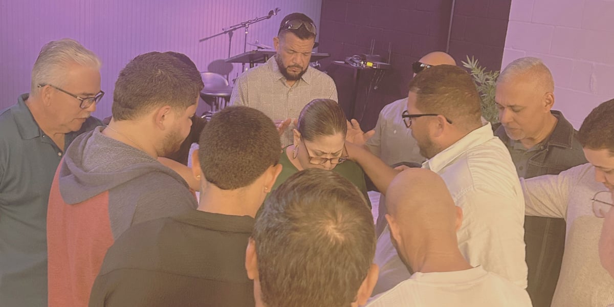 A group of men gathered in a circle during what appears to be a prayer or worship service in a room with purple lighting